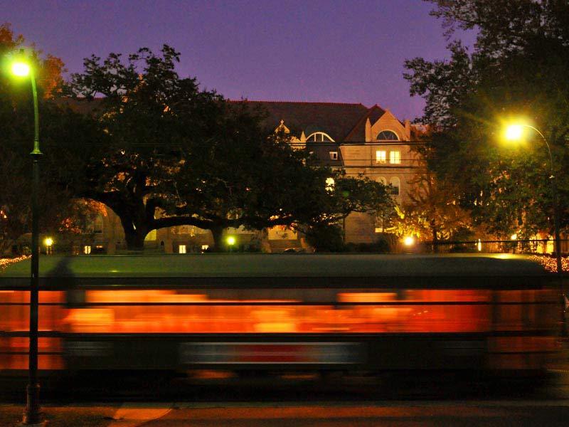 A blurred St. Charles streetcar going past Gibson Hall after twilight.